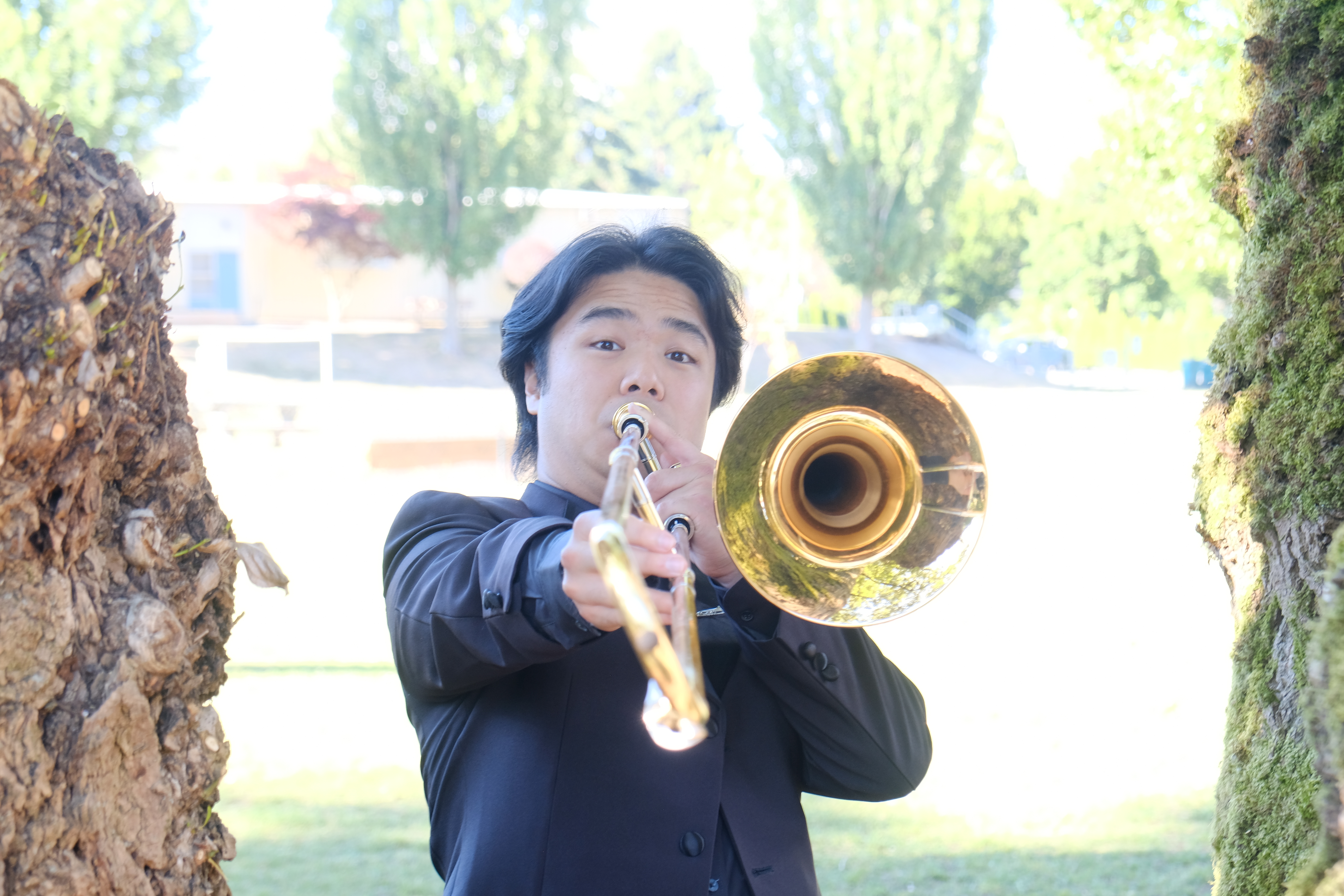 Jobert playing trombone between trees.